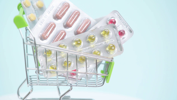Selective focus of spinning shopping cart with pills on blue background  - Footage, Video