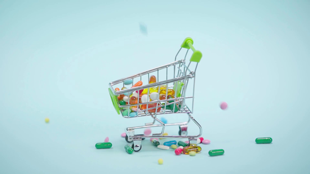 Pillen fallen in kleinen Einkaufswagen auf blauem Hintergrund - Filmmaterial, Video
