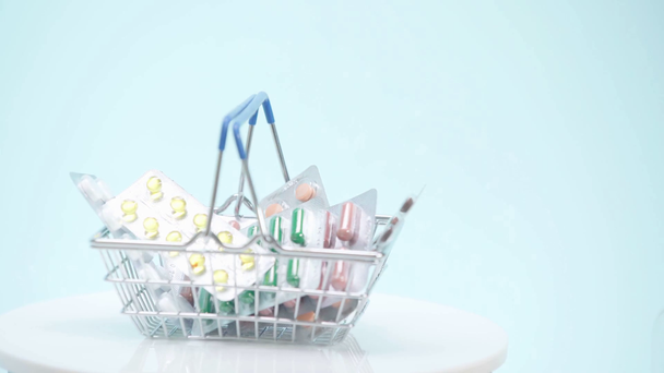 Selective focus of shopping basket with pills on blue background - Footage, Video