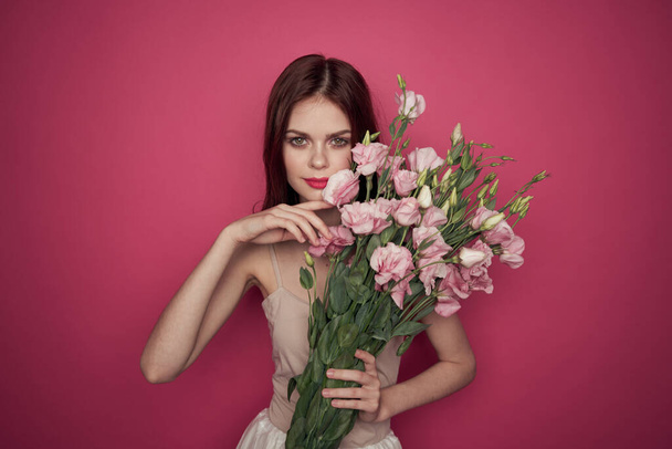 hermosa mujer con un ramo de flores sobre un fondo rosa en un modelo de maquillaje vestido ligero - Foto, imagen