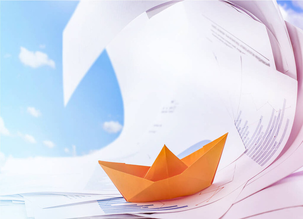 jedna pomarańczowa papierowa łódka unosi się na dokumentach na tle błękitnego nieba. koncepcja działalności gospodarczej - Zdjęcie, obraz