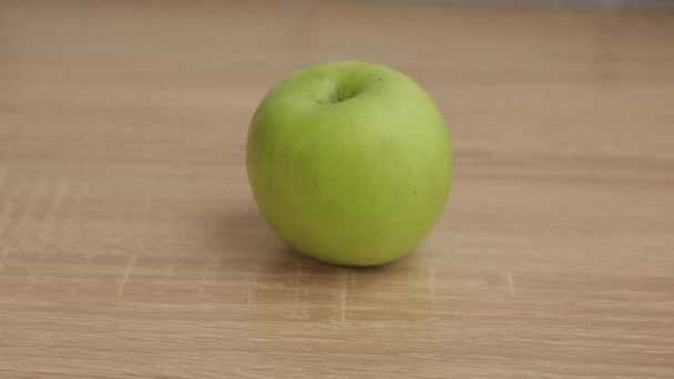 Πράσινο μήλο βρίσκεται στο φως ξύλινο τραπέζι και χωρίζεται στο μισό με το χέρι - Πλάνα, βίντεο