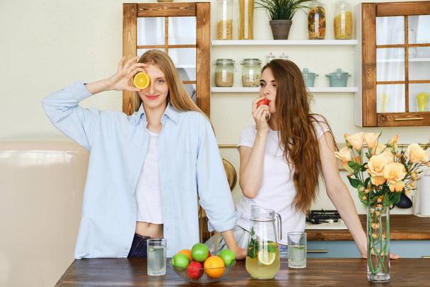 Two beautiful young women eat fruits in the kitchen - Fotoğraf, Görsel