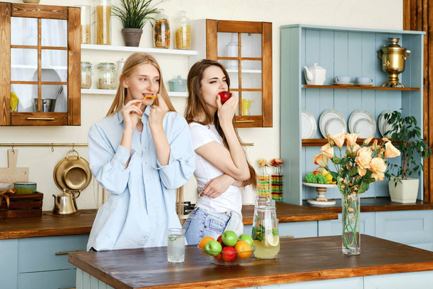Two beautiful young women eat fruits in the kitchen - Fotoğraf, Görsel