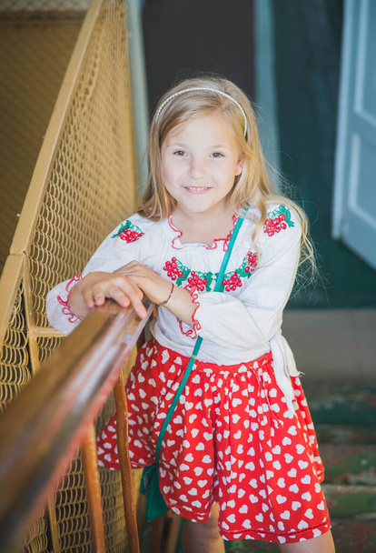 krásná teen dívka v červené sukni s úsměvem stojí na schodech - Fotografie, Obrázek