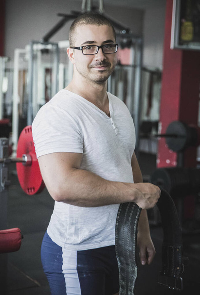 Мускулистый парень в очках держит спортивный пояс в фитнес-клубе - Фото, изображение
