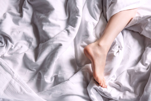 Női láb fehér ágyneműn - Fotó, kép