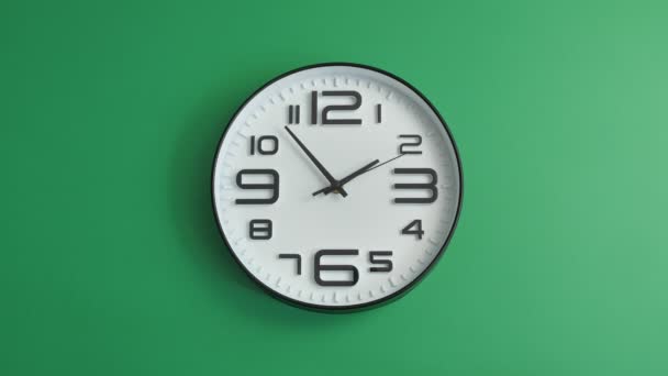 Jednoduché bílé kancelářské hodiny visící na zeleném pozadí - Záběry, video