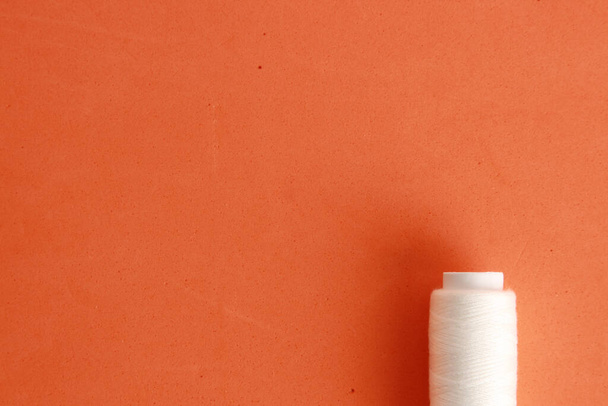A top view of a roll of white sewing thread on an orange background - Фото, изображение