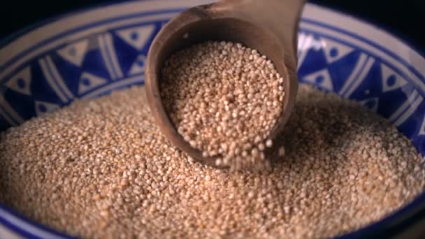Puinen lusikka kaatamalla Kvinoa Siemenet kaunis keraaminen kulho (hidastettuna) - Materiaali, video