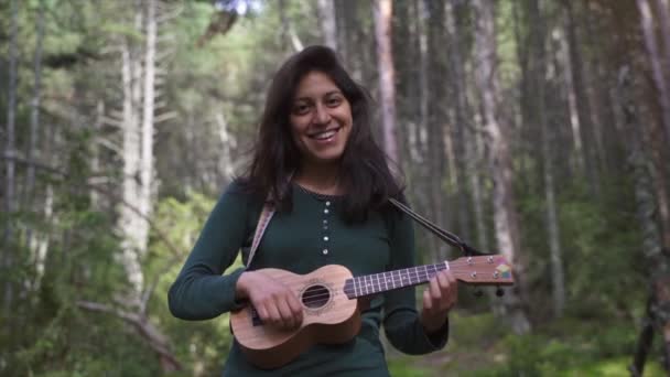 Χαρούμενη Χαμογελαστή Νεαρή Γυναίκα Παίζοντας ένα τραγούδι των Ukelele στη μέση ενός δάσους - Πλάνα, βίντεο