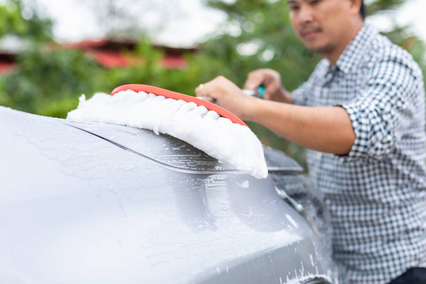 Asian man using white mop with soap to washing the car at outdoor. Car cleaning and maintenance concept - Valokuva, kuva