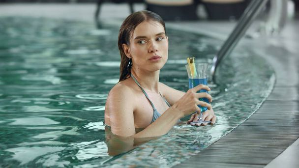 Сексуальная женщина крупным планом выпивает коктейль в бассейне в отпуске. Леди флиртует в бассейне
. - Фото, изображение