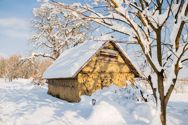 A hut in a field covered in the snow under the sunlight in winter - Photo, Image