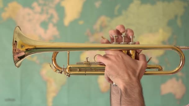 Παγκόσμια Μουσική. Τα χέρια του ανθρώπου παίζουν τρομπέτα μπροστά από έναν παγκόσμιο χάρτη - Πλάνα, βίντεο