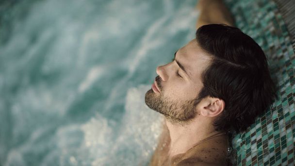 Κοντινό πλάνο σέξι άντρας που απολαμβάνει σπα με τζακούζι. Πορτρέτο του όμορφου άντρα χαλαρώνοντας στην πισίνα - Φωτογραφία, εικόνα