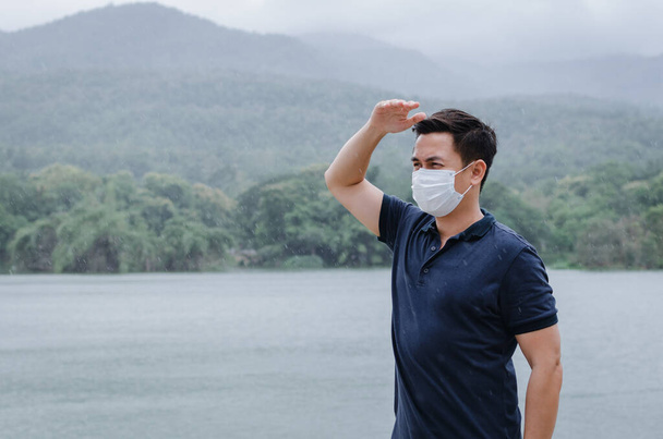 Asiatique homme portant un masque facial pour protéger du virus et se mouiller de la pluie en saison de mousson. - Photo, image