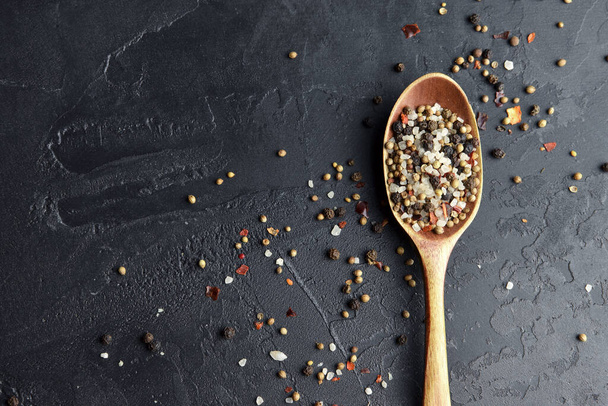 Variety of spices in wooden spoon. Sea salt, mixed pepper, cardamon and mustard seeds on dark black slate background. Top view. Copy space. - Foto, imagen