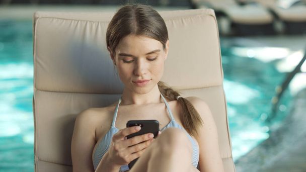 Ritratto di donna sexy rilassante con telefono a bordo piscina. Bella ragazza mobile scorrimento - Foto, immagini