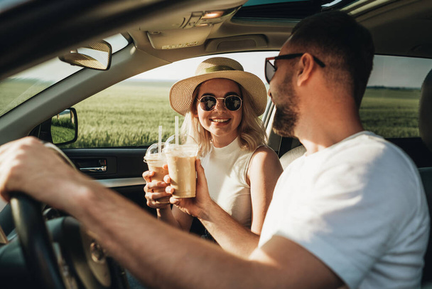 Mężczyzna i kobieta siedzi w samochodzie, pijąc zimną kawę i ciesząc się przygodą Road Trip - Zdjęcie, obraz