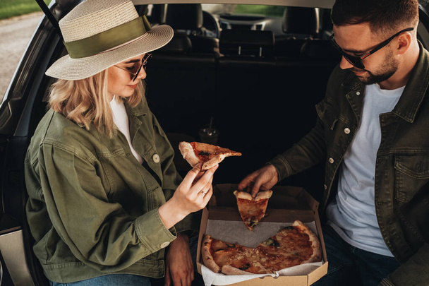 男と女が車のトランクに座ってピザを食べる - 写真・画像