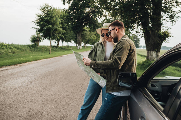 Άνδρας και γυναίκα Νέοι ταξιδιώτες χρησιμοποιώντας το χάρτη κοντά στο αυτοκίνητο στο οδικό ταξίδι - Φωτογραφία, εικόνα