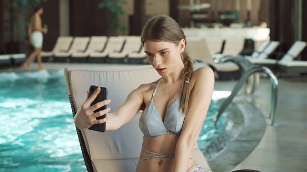 Porträt einer jungen Frau macht Selfie auf Liege in Schwimmbadnähe. - Foto, Bild