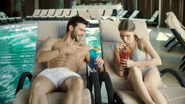 Een hecht stel dat cocktails drinkt in ligstoelen. man en vrouw ontspannen samen - Foto, afbeelding