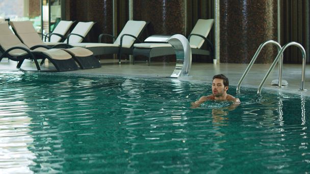 豪華なホテルでリラックスした男がプールサイドを歩いています。プールで一人で泳ぐ男. - 写真・画像