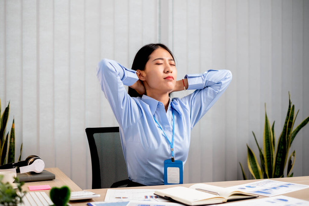 Aasian naispuolinen kirjanpitäjä on väsynyt työskentelemästä tuolissa, venyttelemästä rentoutumaan ja rentoutumaan työskennellessään ahkerasti toimistossa.. - Valokuva, kuva