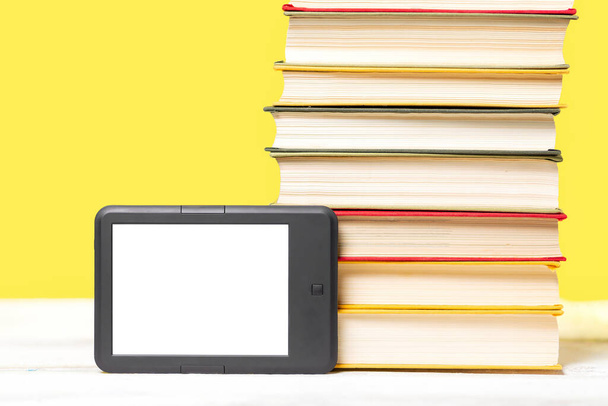 E-Learning. E-Book-Reader und ein Stapel Bücher auf gelbem Hintergrund. Attrappe auf. Kopierraum. Konzept der Bildung und elektronischer Geräte. - Foto, Bild