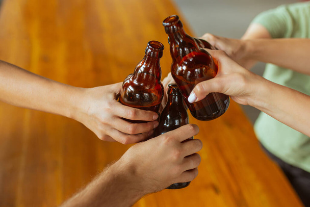 Young group of friends drinking beer, having fun, laughting and celebrating together. Close up clinking beer bottles - Foto, Imagem