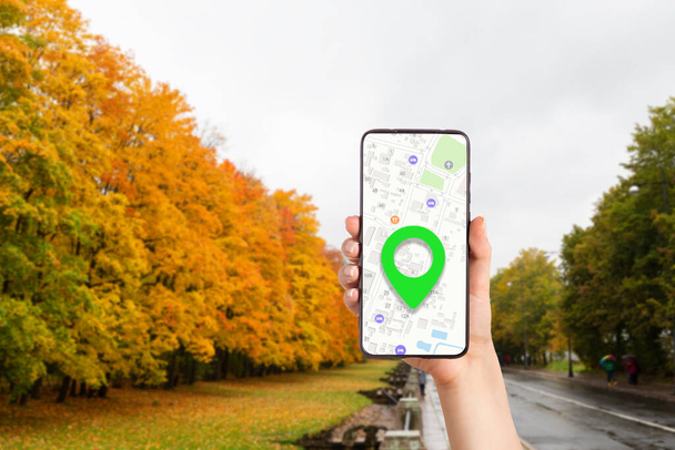 Dişi bir el, hedef işaretli online harita uygulaması olan bir akıllı telefonu tutuyor. Arka planda bir sonbahar parkı var. İnternet gezinti ve modern teknolojiler kavramı - Fotoğraf, Görsel