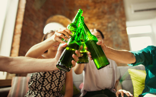Young group of friends drinking beer, having fun, laughting and celebrating together. Close up clinking beer bottles - Photo, image