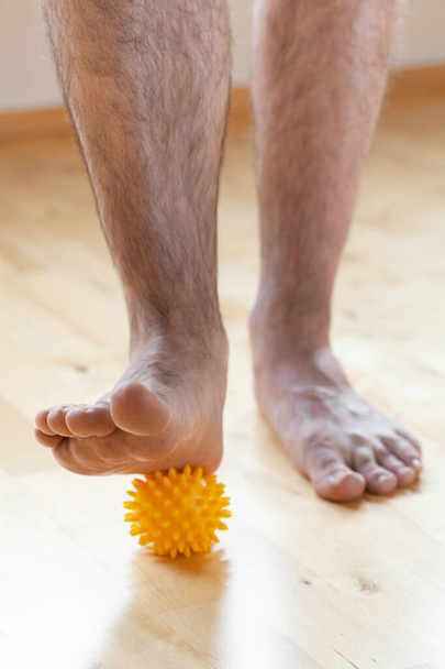 hombre haciendo ejercicio gimnástico de corrección de pie plano usando bola de masaje en casa - Foto, Imagen