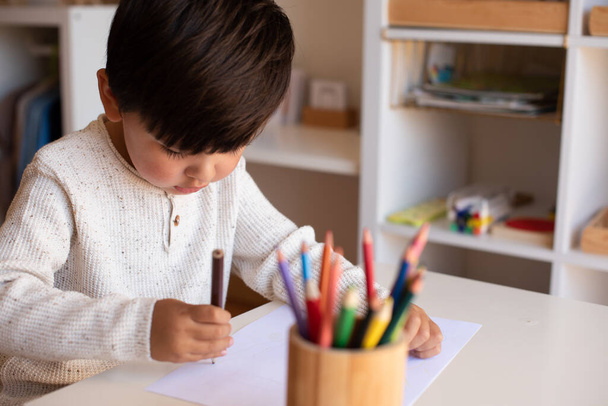 Ένα μικρό παιδί που ζωγραφίζει με χρωματιστά μολύβια. Μαθήματα κατ 'οίκον. Μαθαίνοντας κοινότητα. Σχολή Μοντεσόρι.  - Φωτογραφία, εικόνα