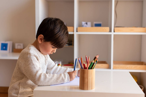 Um miúdo pré-escolar a desenhar com lápis de cor. A estudar em casa. Comunidade de aprendizagem. Escola Montessori.  - Foto, Imagem