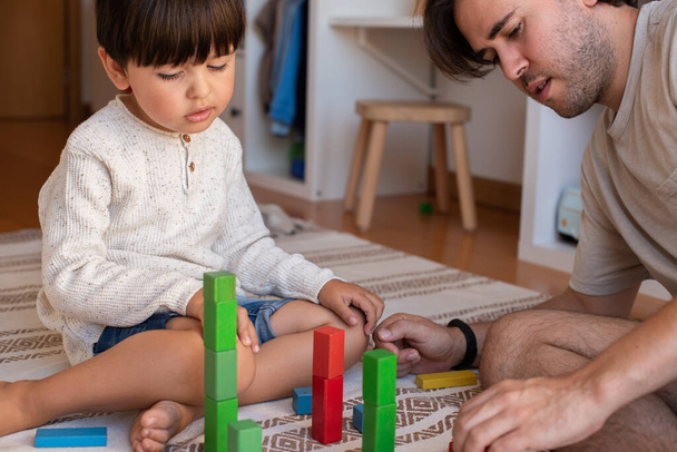 Το μικρό παιδί και ο πατέρας του παίζουν στο σπίτι με ξύλινα δοκάρια. Μαθήματα κατ 'οίκον. Μείνε σπίτι. Οικογενειακός χρόνος - Φωτογραφία, εικόνα