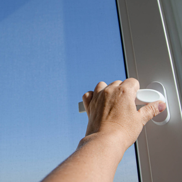 Woman's hand opens the handle of a plastic window against a blue sky - Photo, Image