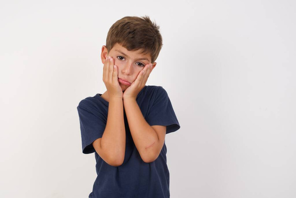 Beautiful kid boy wearing casual t-shirt standing over isolated white background,. Tired hands covering face, depression and sadness, upset and irritated for problem - Fotografie, Obrázek