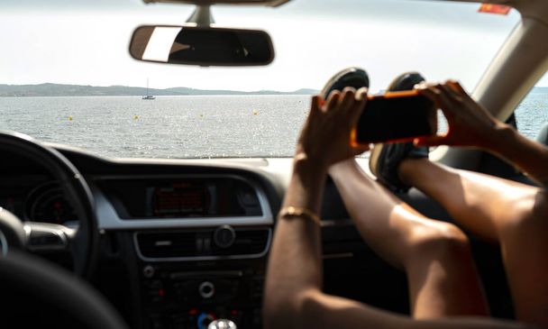 woman's hands inside a car taking photos traveling, on the beach - Photo, Image