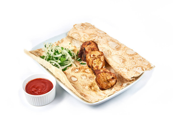 Kebab de poulet avec sauce dans un restaurant. Brochettes avec oignons et pain pita sur une assiette blanche. Servant des plats dans un café, un restaurant, pour un menu. Isolé sur fond blanc - Photo, image