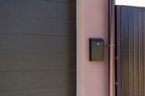 Ein brauner Briefkasten an der rosafarbenen Wand neben dem Fallrohr. Die Garagentore sind links mit Schutzrollläden verschlossen. Immobilien und Architektur. - Foto, Bild