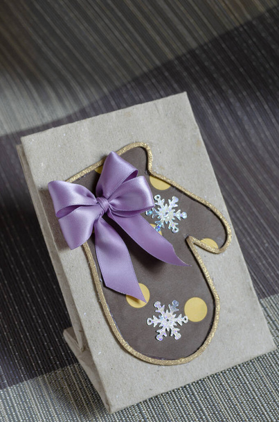 Házi készítésű karácsonyi ajándéktáska lila masnival és kesztyűvel. Papírzacskó a hagyományos ajándékokhoz. Felülnézetből, szögből. Szelektív fókusz. - Fotó, kép