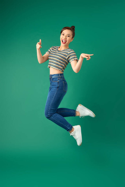 幸せな正の若いアジアの女性の肖像画ジャンプし、手を振って緑の背景. - 写真・画像