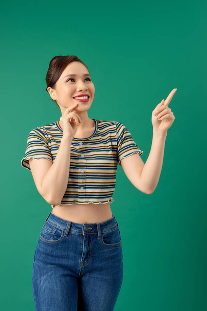 Smiling happy young Asian woman pointing her hand over green background. - 写真・画像
