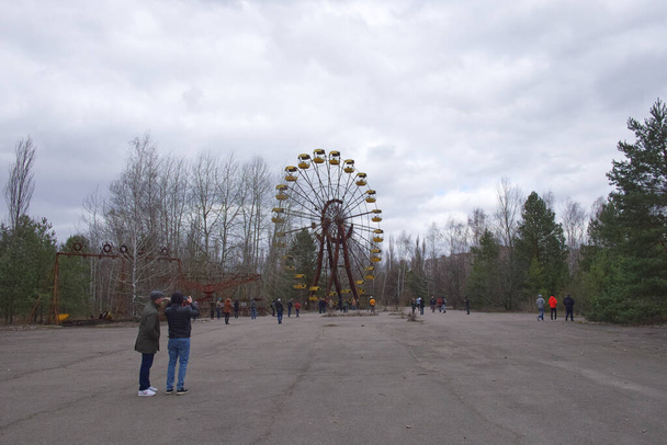 Pripyat, Ukraine, 14 mars 2020. Touristes près de la célèbre grande roue dans un parc d'attractions abandonné à Pripyat. Météo nuageuse, le ciel est couvert de nuages. - Photo, image