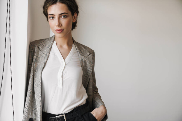 Photo of confident successful woman in jacket looking at camera while posing at white office - Foto, immagini