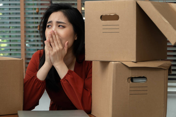 Szomorú ázsiai nő pakolja a holmiját egy kartondobozba és sír az asztalon az irodában, miután elbocsátották és munkanélküli lett. A gazdasági visszaesésre gyakorolt hatás fogalma és a kudarc kezelése - Fotó, kép