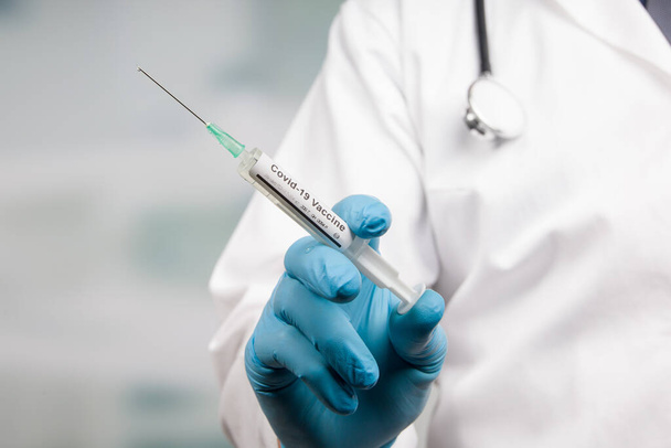 lähikuva lääkärin kädestä lääkekäsineissä Covid-19-rokotteella varustetulla ruiskulla - Valokuva, kuva
